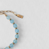 Détail du fermoir en acier inoxydable doré et du pendentif Komète Atelier sur le bracelet Kaleb en perles d’eau douce et aigue-marine naturelles.