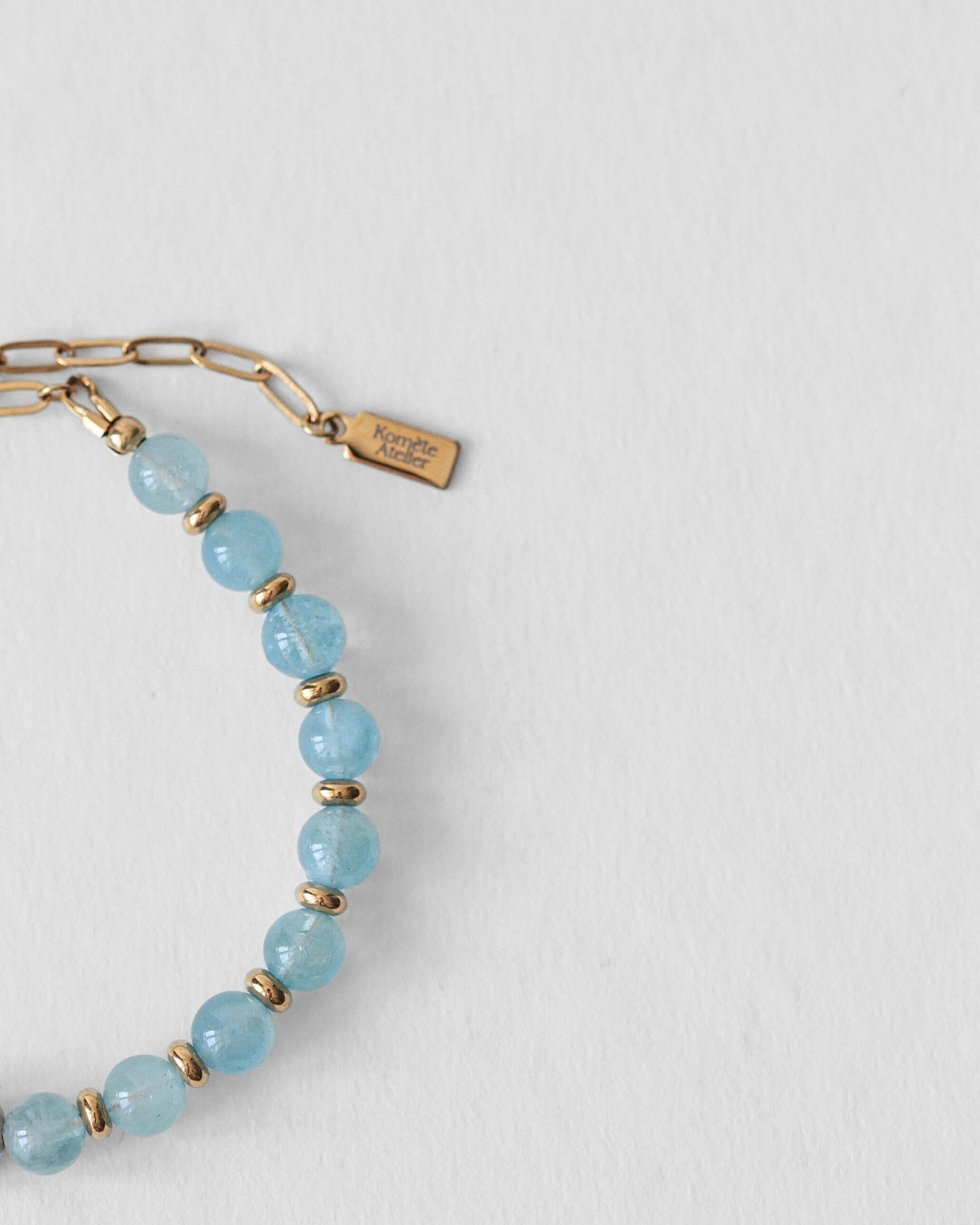 Détail du fermoir en acier inoxydable doré et du pendentif Komète Atelier sur le bracelet Kaleb en perles d’eau douce et aigue-marine naturelles.
