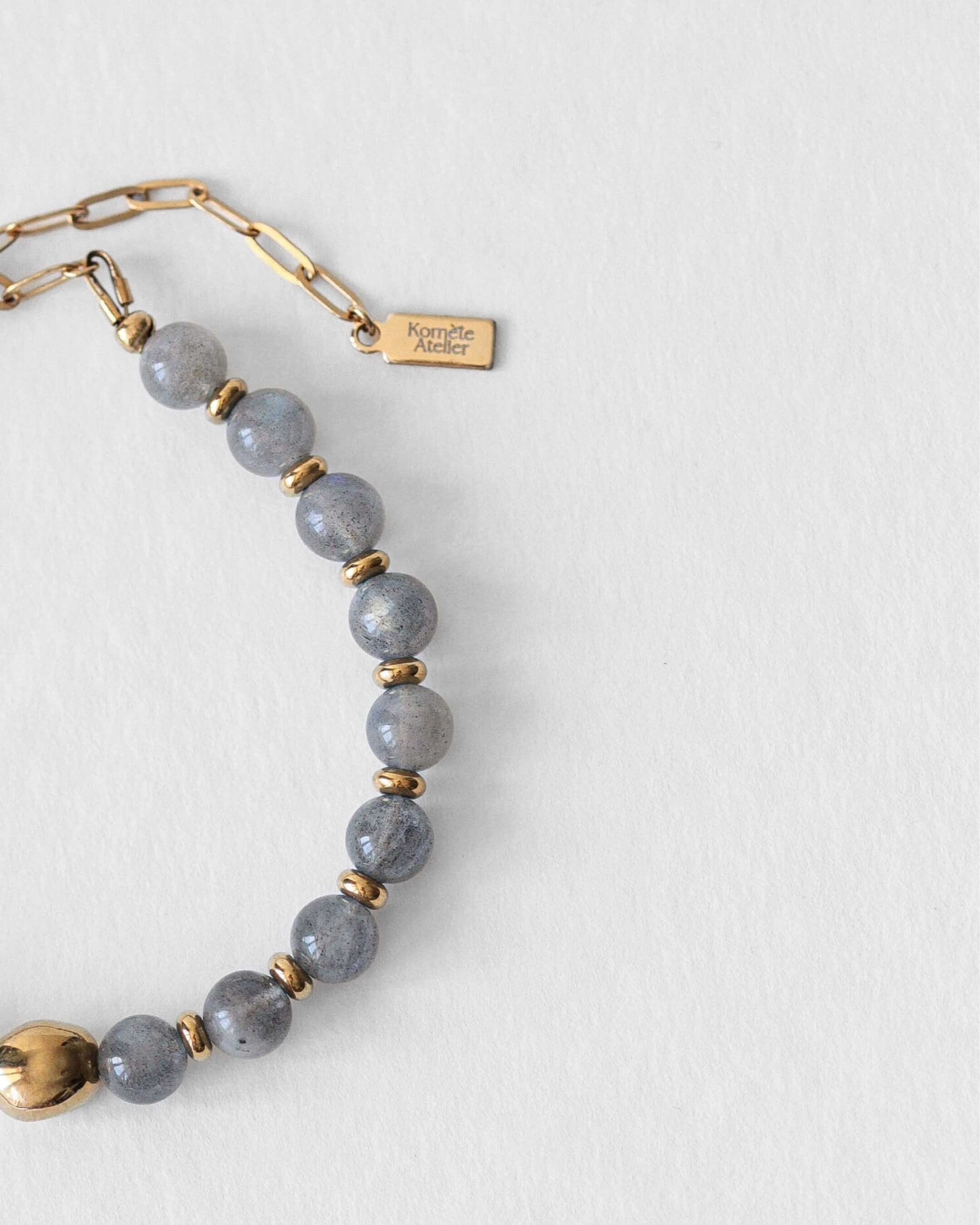 Détail du fermoir en acier inoxydable doré et du pendentif Komète Atelier sur le bracelet Kaleb en perles d’eau douce et labradorite naturelles.