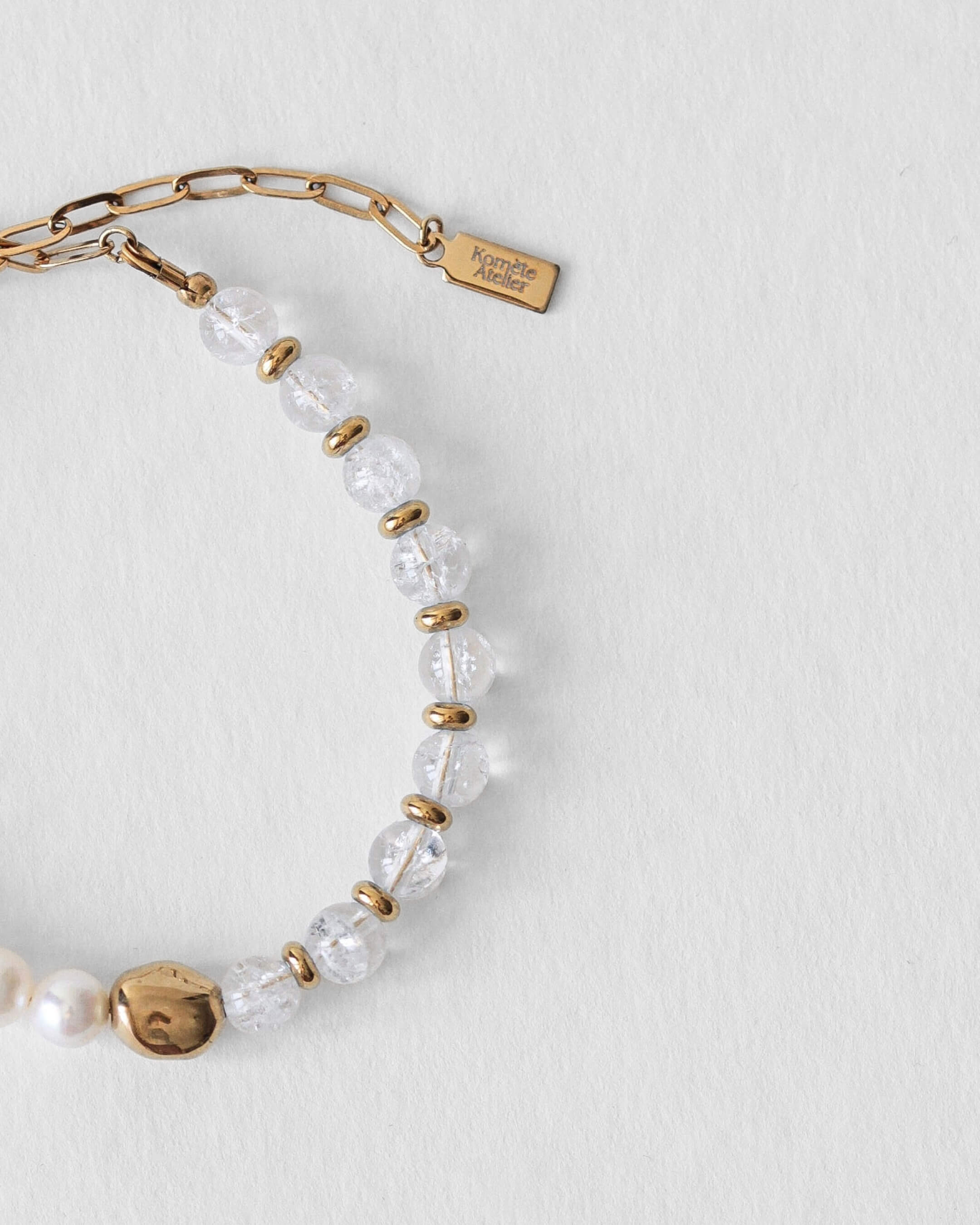 Détail du fermoir en acier inoxydable doré et du pendentif Komète Atelier sur le bracelet Kaleb en perles d’eau douce et quartz craquelé naturel.
