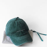 Casquette Komète Atelier gris foncé posée sur pochette cadeau Komète Atelier avec ruban vert