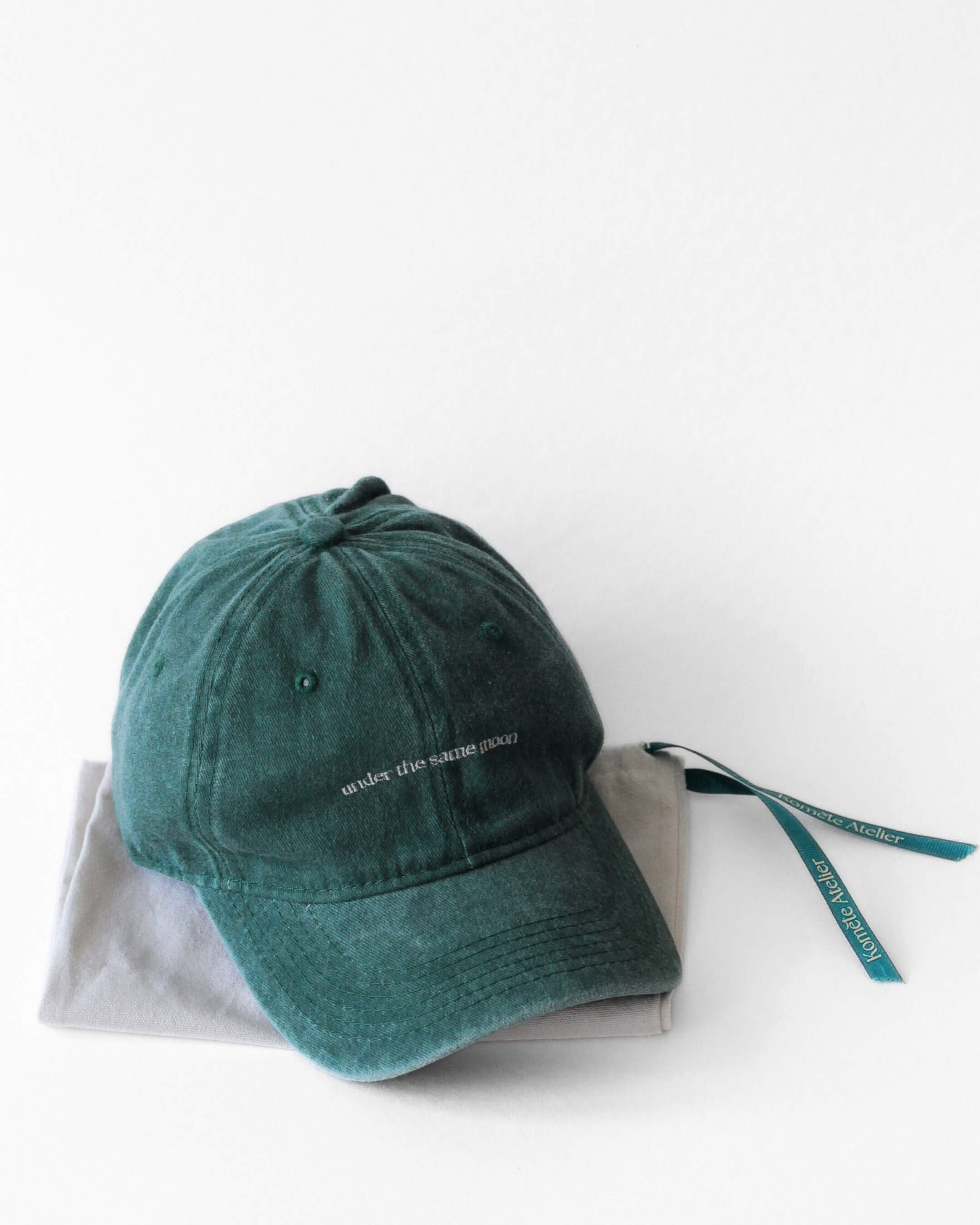 Casquette Komète Atelier gris foncé posée sur pochette cadeau Komète Atelier avec ruban vert