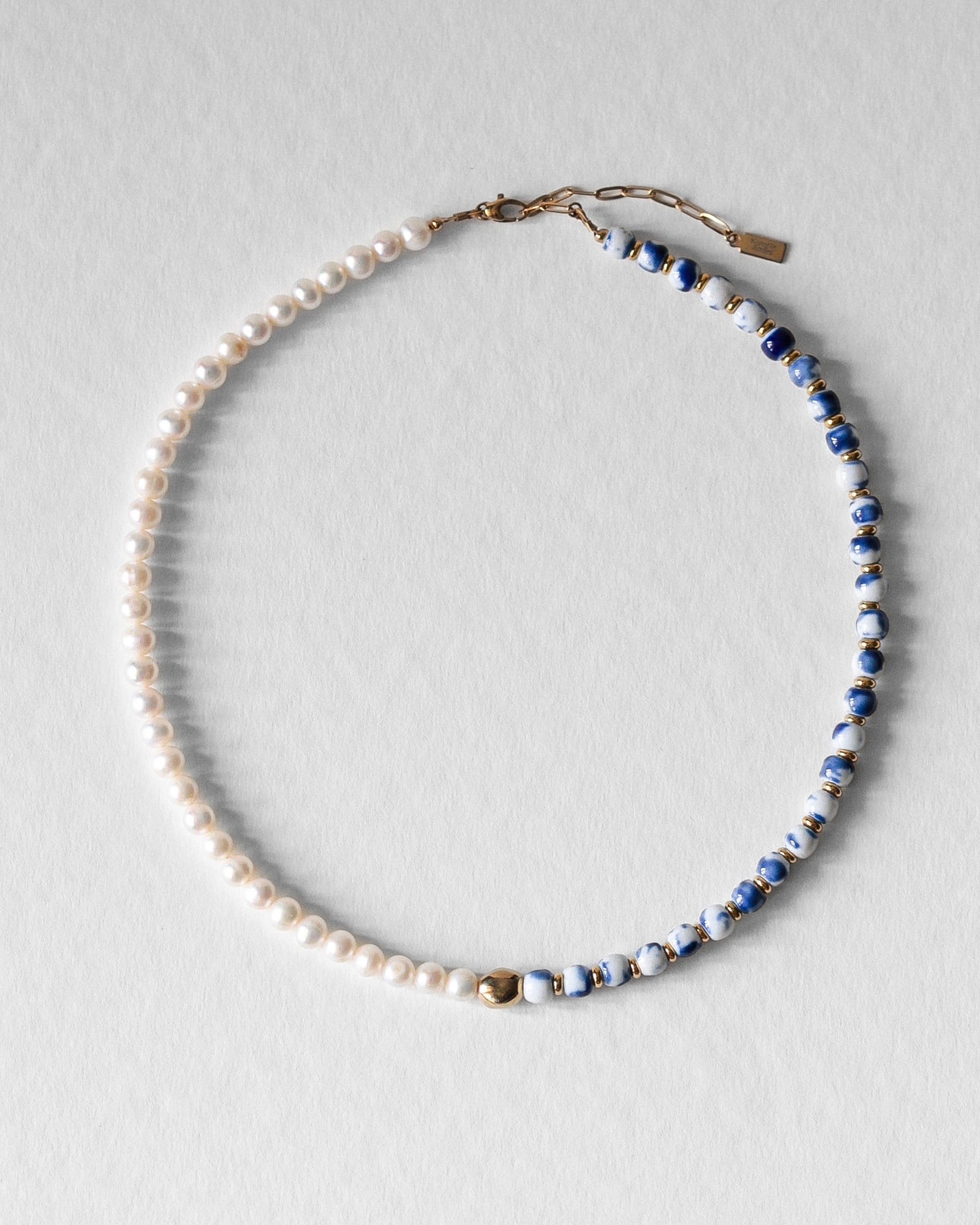 Collier Kaleb en perles de porcelaine bleue et perles d’eau douce, aussi appelées perles de culture, monté sur acier inoxydable doré. Bijou artisanal fait main Komète Atelier, collier élégant unisexe pour homme et femme en céramique et perles de culture.